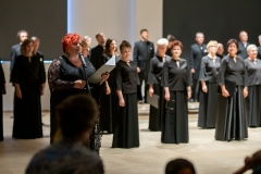 Chór Filharmonii Śląskiej na scenie Łaźni,  kobieta trzymająca teczkę (Regina Gowarzewska) zapowiadająca koncert przy mikrofonie