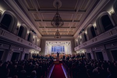 Sala koncertowa im. Karola Stryji wypełniona melomanami, w oddali estrada, zabytkowe  żyrandole, orkiestra na estradzie