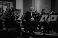 Czarno-białe zdjęcie. Solista koncertu Rainer Honeck na scenie, prowadzący orkiestrę  pulpitu koncertmistrza.