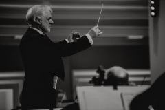Czarno-białe zdjęcie. Solista koncertu Rainer Honeck z batutą, prowadzący orkiestrę.