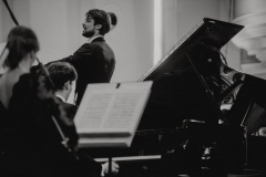 Czarno-białe zdjęcie. Dyrygent Yaroslav Shemet widoczny zza muzyków orkiestry.