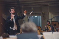 Dyrygent Yaroslav Shemet widoczny zza muzyków orkiestry.