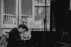 Czarno-białe zdjęcie. Solista koncertu Szymon Nehring przy fortepianie.