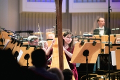 Agnieszka Kaczmarek-Bialic przy harfie na scenie, za nią Orkiestra Symfoniczna Filharmonii Śląskiej