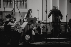 Czarno-białe zdjęcie. Orkiestra, solistka Bożena Bujnicka oraz Mirosław Jacek Błaszczyk widoczny od tyłu
